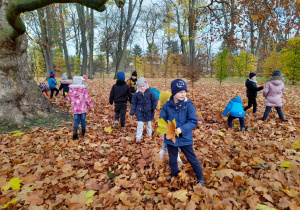 Dzieci chodzą po jesiennym dywanie z liści w parku.