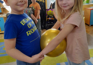 Kacper i Lena tańczą z balonem przy muzyce trzymając go między brzuchami.
