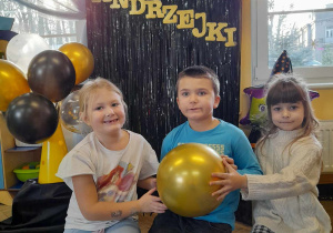 Anastazja, Gabryś i Zosia pozują do zdjęcia ze złotym balonem na tle dekoracji andrzejowej.