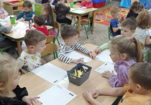 Dzieci siedzą przy stolikach i rysują swojego nowego misia Milusia.