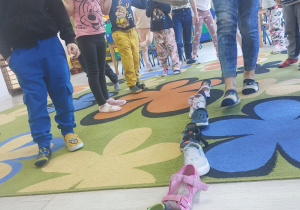 Dzieci stoją w rozsypce na dywanie, na podłodze ustawione są buty dzieci .