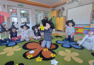Przedszkolaki siedzą w kole na dywanie .W środku koła rozłożone są żółte gwiazdki. Chłopiec w środku koła pokazuje gwiazdkę na której jest gałązka.