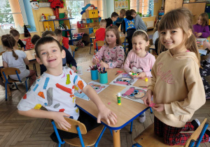 Dzieci z grupy Słoneczek siedzą przy stolikach w trakcie tworzenia pracy plastycznej