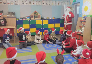 Przedszkolaki siedzą na dywanie, w drzwiach pojawia się Święty Mikołaj