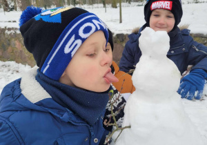 Kacper w wyjętym językiem udaje, że zamierza polizać śniegowego bałwanka