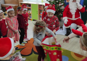 Dzieci stoją w kole, a Amelka odbiera od Mikołaja torbę z zabawkami dla grupy.