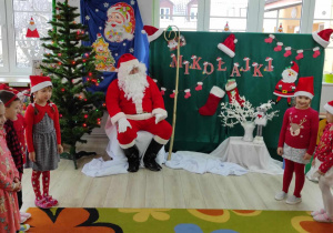 Mikołaj siedzi na wprost, a z boków stoją dzieci z grupy „Biedronek” i śpiewają piosenkę.