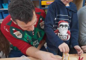 Julek razem ze swoim tatą ozdabia kolorowymi posypkami chatkę wykonaną z muffinki, kremu i ciasteczek.