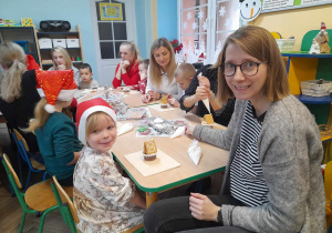 Dzieci siedzą przy stolikach razem z rodzicami i wykonują chatkę z muffinki, kremu i ciasteczek. Łucja razem z mamą prezentują swoją chatkę.