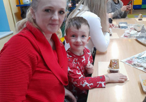 Bartuś siedzi przy stole obok mamy. Przed chłopcem na deseczce leży świąteczna chatka z muffinki.