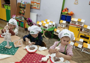 Grupka dzieci wyciskają biały lukier dekorując pierniki.
