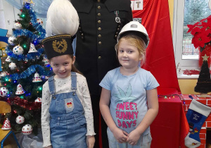 Dwie dziewczynki pozują do zdjęcia razem z górnikiem. Julka ma głowie czapkę górniczą, a Anastazja kask. W tle dekoracja świąteczna.