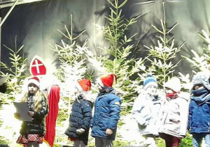 Pięcioro dzieci stoi na scenie podczas wręczania dyplomu i upominków. W tle dekoracja świąteczna, Mikołaj.