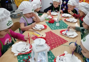 Grupka przedszkolaków dekorują ciasteczkowe Mikołaje kolorowymi lukrami.