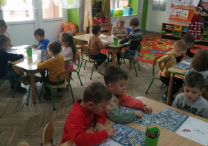 Przedszkolaki siedzą przy stolikach i wykonują zadanie: naklejają prezenty w liście do Mikołaja.