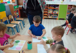 Dzieci przy stolikach kolorują kredkami koła narysowane na kartce. Pani Ewa obserwuje pracę dzieci.