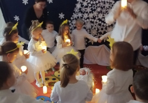 Dzieci tworzą dwa koła: chłopcy na zewnątrz trzymają się za ręce, w środku dziewczynki z podniesionymi do góry płonącymi świecami.