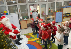 Przedszkolaki występują przez Mikołajem, który siedzi na wcześniej przygotowanym dla niego krześle. Dzieci śpiewają piosenkę.