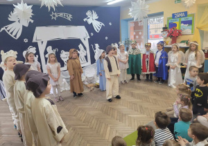 Dzieci stoją w półkolu, a na środku sceny stoi Franek. Przedszkolaki śpiewają pastorałkę "Ach, co za noc".