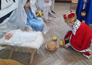 Eryk w roli Króla kładzie złoto przy żłóbku, w którym leży dzieciątko. Przed nim siedzi Zosia w roli Maryi.