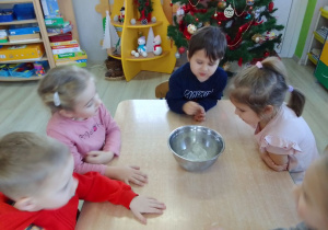 Dzieci obserwują kostki lodu umieszczone w metalowej misce.