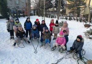 Zdjęcie grupowe dzieci z grupy "Motylki" z sankami w ogrodzie przedszkolnym.