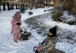 Marysia ciągnie sanki, na których siedzi Tosia.