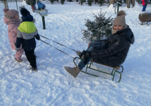 Mikołaj i Marysia ciągną sanki, na których siedzi pani.