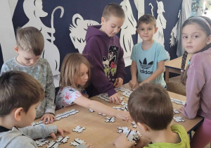 Przedszkolaki siedząc przy stolikach układają puzzle, tworząc ścieżki dla Ozobotów.