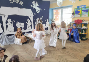 Dziewczynki z grupy "Słoneczek" przebrane za aniołki i gwiazdki tańczą w parach. Z tyłu siedzi Kacper w stroju Józefa.