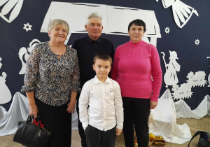 Gabryś z dwoma Babciami i Dziadkiem pozują do zdjęcia na tle jasełkowej dekoracji.