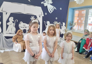 Ala, Winek i Łucja w białych sukienkach stoją przed publicznością. Po prawej widać Eryka i Gabrysia w strojach królów.