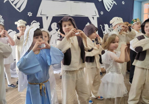 Dzieci z grupy "Słoneczek" stoją na scenie z dłońmi ułożonymi w kształt serduszka.