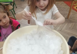 Emma za pomocą łyżki wkłada śnieg z miski do foliowej torebki.
