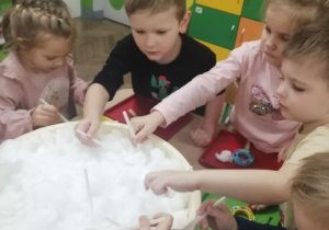 Grupka dzieci za pomocą łyżek nakłada śnieg z miski na tacki.