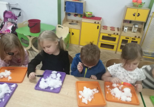 Grupka dzieci ogląda śnieg przez lupę.