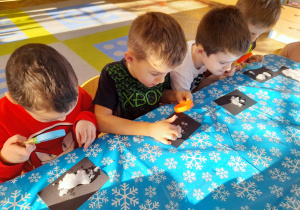 Czterech chłopców siedzi przy stole i ogląda śnieg przez lupy.