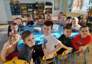 Dzieci siedzą przy złączonych stołach, na których leży niebieska ceratka w śnieżynki i stoją dwie miski ze śniegiem.