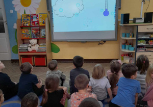 Dzieci siedzą przed tablicą multimedialną i ogladają film edukacyjny "Jak powstaje śnieg?".