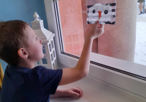 Tomek stoi przy oknie i dotyka foliowego woreczka, w którym roztapia się bałwanek ze śniegu.