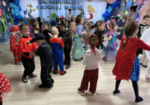 Dzieci w strojach balowych swobodnie tańczą przy muzyce.