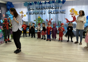 Pani Angelika tańczy na środku sali, a za nią dzieci razem z Panią dyrektor. W tle dekoracja balowa.
