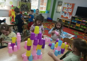 Dziewczynki ustawiają wieżę według własnego pomysłu w kolorze różowym , fioletowym, żółtym i niebieskim.