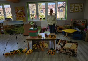 Na zdjęciu pani Justyna, plansze z ilustracjami, ul, plastry miodu, słoiki z miodem i kwiaty słonecznika które leża na stoliku.