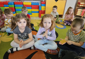 Dzieci z grupy "Motylki" siedzą na dywanie trzymając w dłoniach plastry wosku.