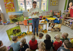 Pani Justyna stoi przed dziećmi i pokazuje plaster wosku pszczelego.