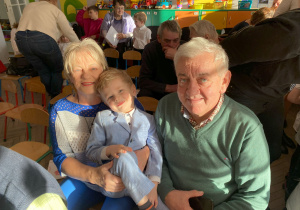 Uśmiechnięty Olek pozuje do zdjęcia ze swoimi dziadkami.