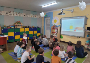 Dzieci z grupy Słoneczek siedzą na dywanie i oglądają film edukacyjny o właściwościach wody