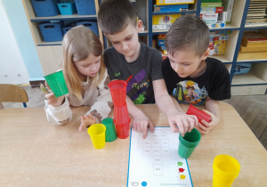 Oskar, Franek i Lena wykonują przedstawione na karcie działania. Dzieci rozpoczęli budować wieżę według kodu i planują dalszą pracę zgodnie z kartą wzoru.