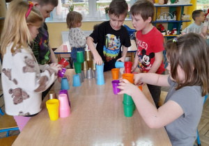Grupka dzieci buduje z kolorowych kubków dowolne konstrukcje.